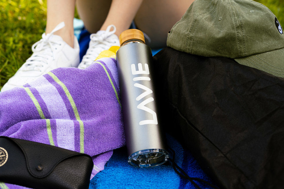 College student on a blanket outside with a purple towl and silver LaVie2Go purified water bottle.
